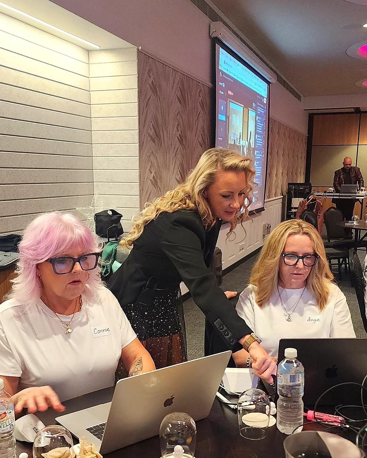 Sarah Cordiner leaning between two business owners, helping them at their laptops