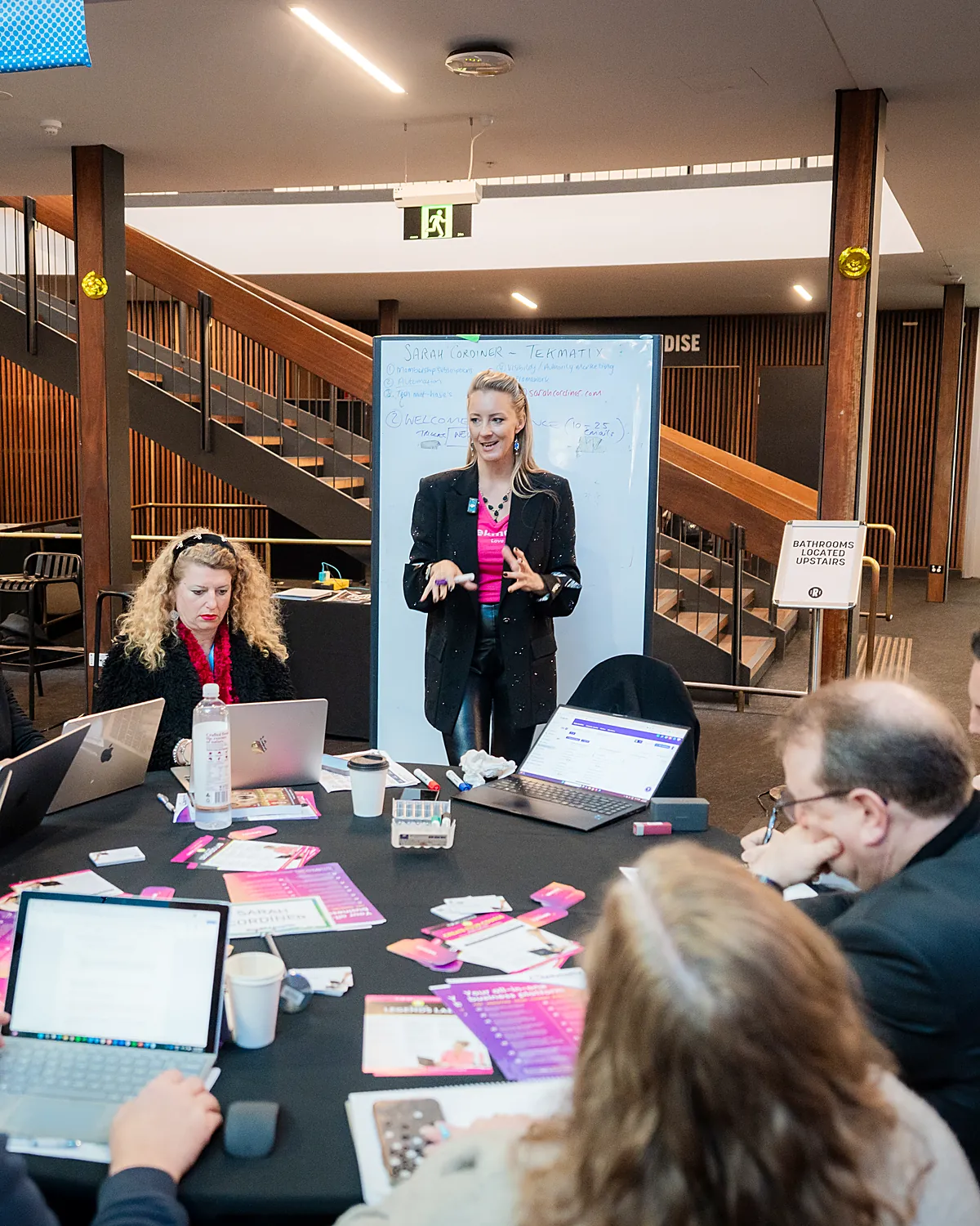 Sarah Cordiner running a hands-on AI session around a boardroom table of laptops