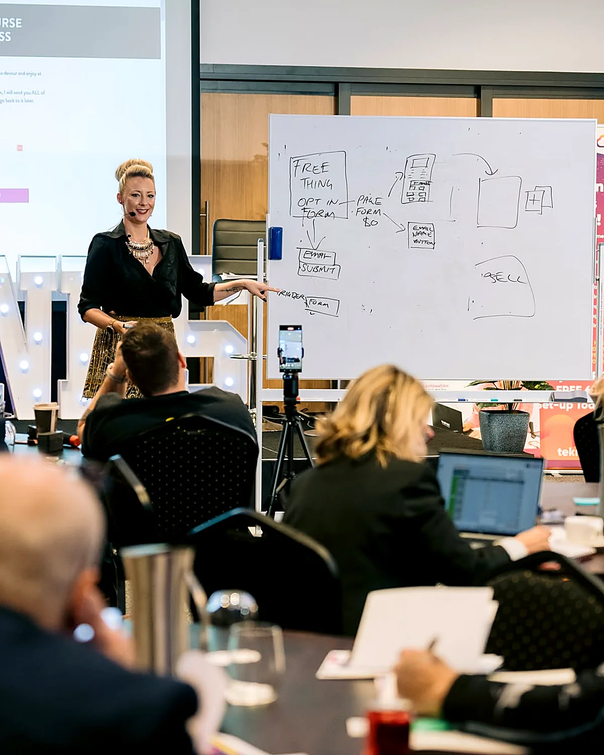 Sarah Cordiner mapping out an automation on a whiteboard for a room of business owners on laptops